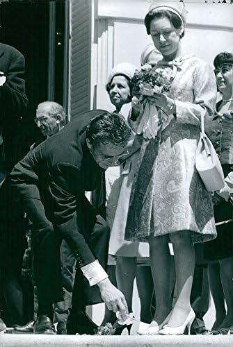 Foto vintage da princesa Margaret, condessa de Snowdon segurando buquê e homem pegando folhas do chão.